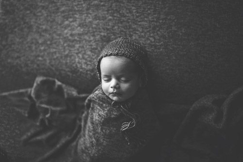 Newborn baby swaddled in textured grey blanket, captured in black and white by a Canberra newborn photographer, highlighting peaceful slumber