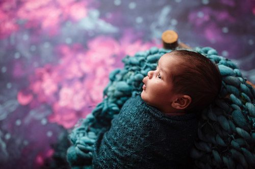 Side view of a newborn in teal wrap, gazing curiously against a pink floral background, captured by a Canberra newborn photographer