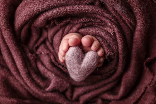 Close-up of newborn feet, perfectly captured by a Canberra newborn photographer, with soft pink and purple hues enhancing the tender moment