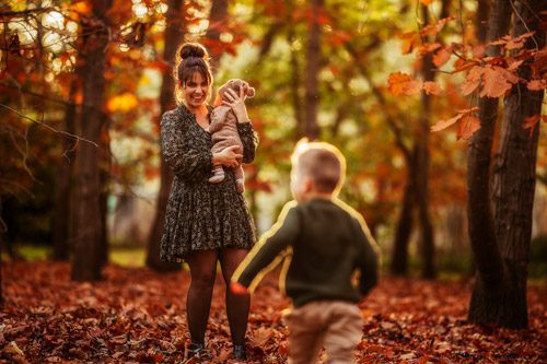 Mother laughs holding her baby as her son runs towards her in a lively family session with a winter Canberra family photographer.
